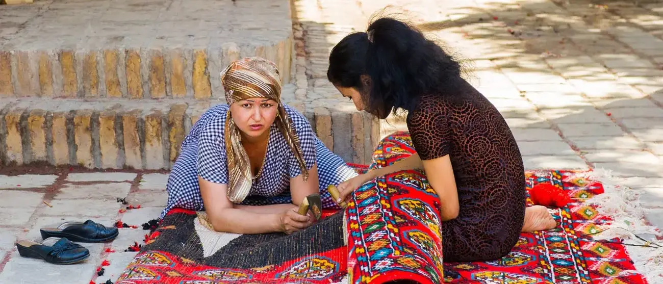 Duas mulheres uzbequestans estão trabalhando em um tapete  