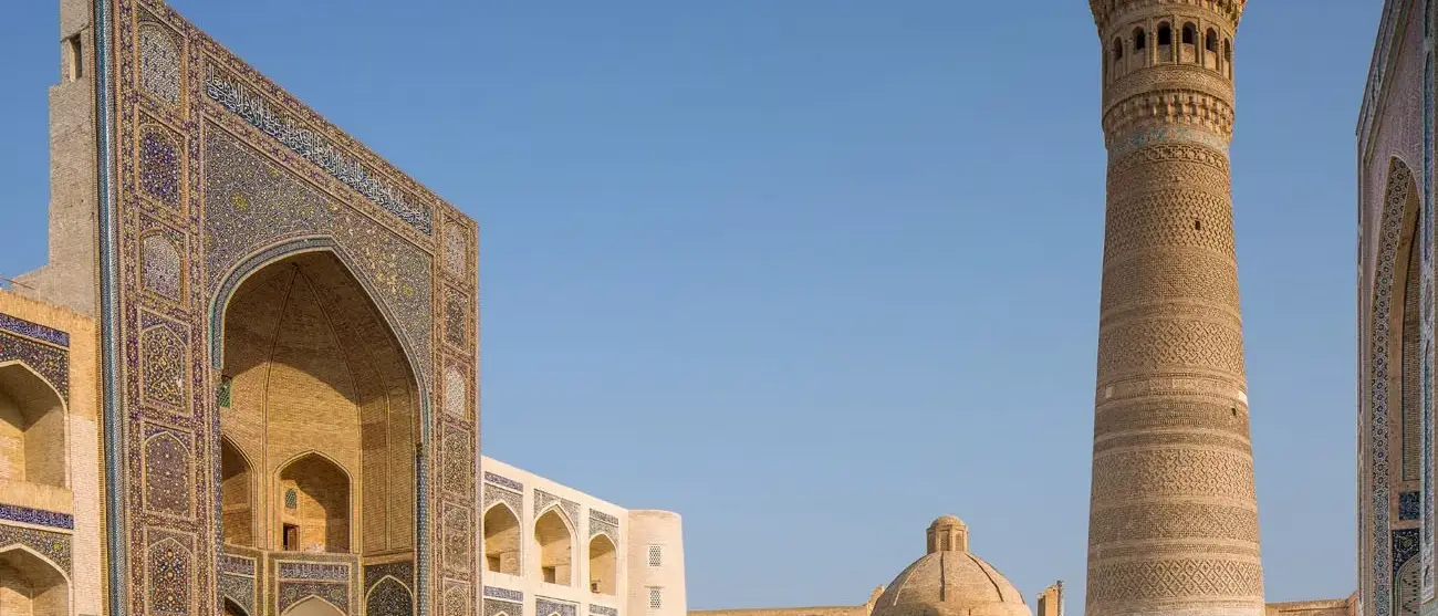 Exterior de Mir-i-árabe Medressa e Kalon Minaret. Dois turistas estão sentados na entrada para Kalon Mosque. Foto tomada em Bukhara, no Uzbequistão.